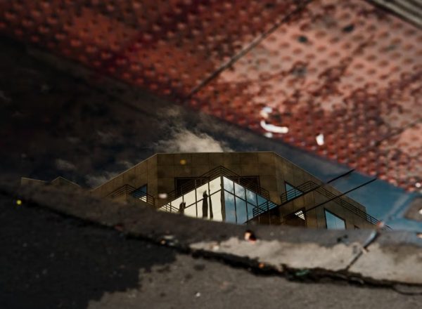 Reflection of a modern architectural building in a sidewalk puddle with textured surfaces.