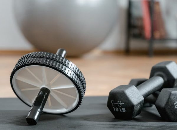 Close-up of ab wheel and dumbbells on a mat in a home gym setting.